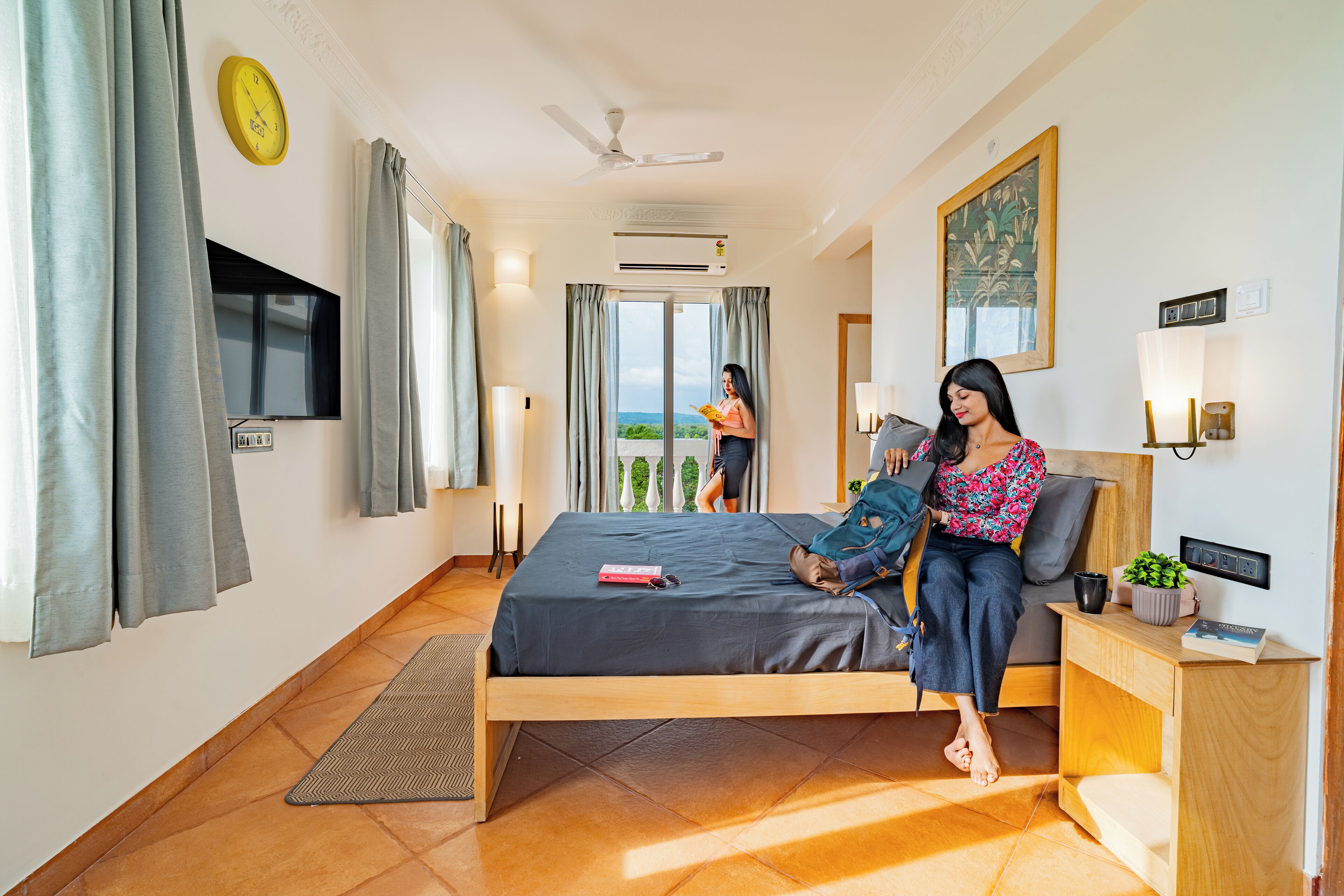 Une chambre d’hôtel moderne, équipée d’un lit, d’une table de chevet avec une lampe, d’un téléviseur fixé au mur et d’une grande fenêtre avec des rideaux.