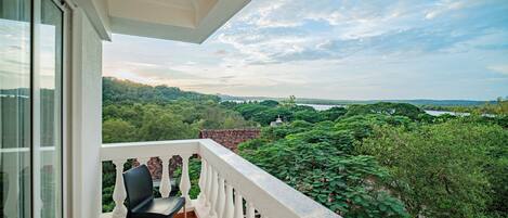 Uma varanda com cadeira, vista para o verde e paisagem distante.