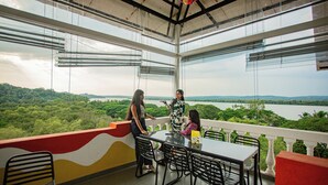 A balcony with a table and chairs overlooking a lush landscape. - The Hosteller Goa, Old Goa (Panaji)
