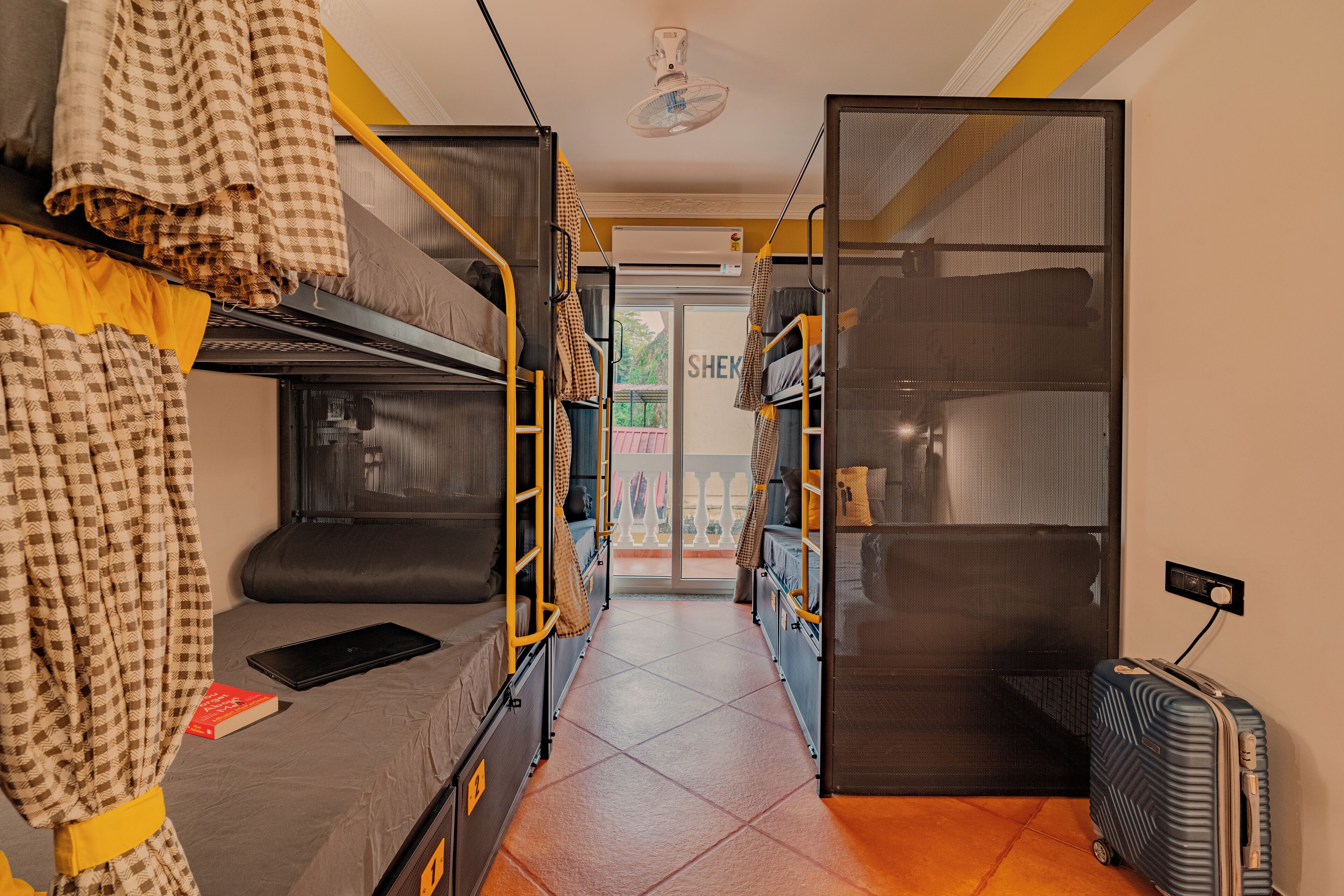 A dormitory room with bunk beds, a small desk, and a suitcase.