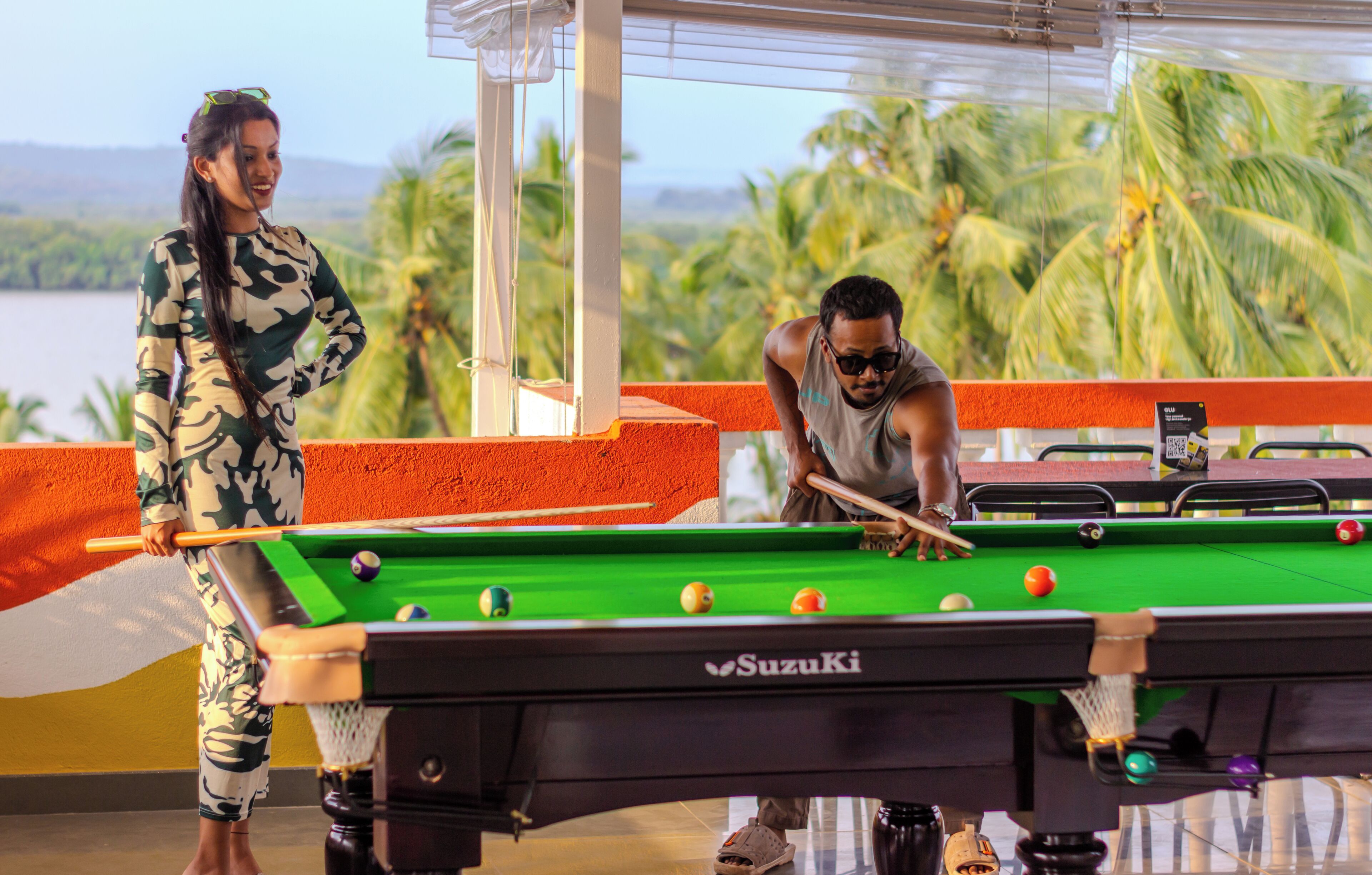 Une table de billard recouverte d’un drap vert, une personne tenant un bâton de billard et une autre personne se tenant à côté de la table.