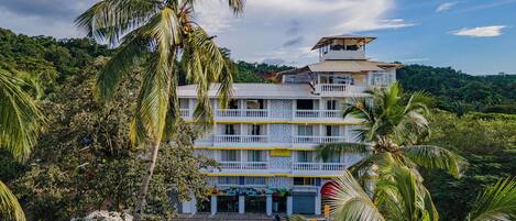 A multi-story building with a restaurant on the ground floor, surrounded by lush greenery and palm trees.
