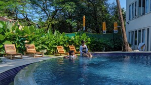 A swimming pool with wooden lounge chairs and a tropical backdrop. - The Hosteller Goa, Old Goa (Panaji)