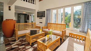 A spacious living area with wooden furniture, a large vase with flowers, and a laptop on a glass table. - The Hosteller Goa, Old Goa (Panaji)
