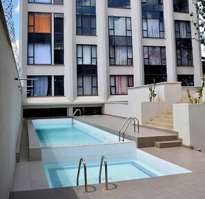 A modern building with a swimming pool, multiple windows, and a staircase leading to an upper level. - Lavish Apartment With Swimming Pool Ongata Rongai (Ongata Rongai)