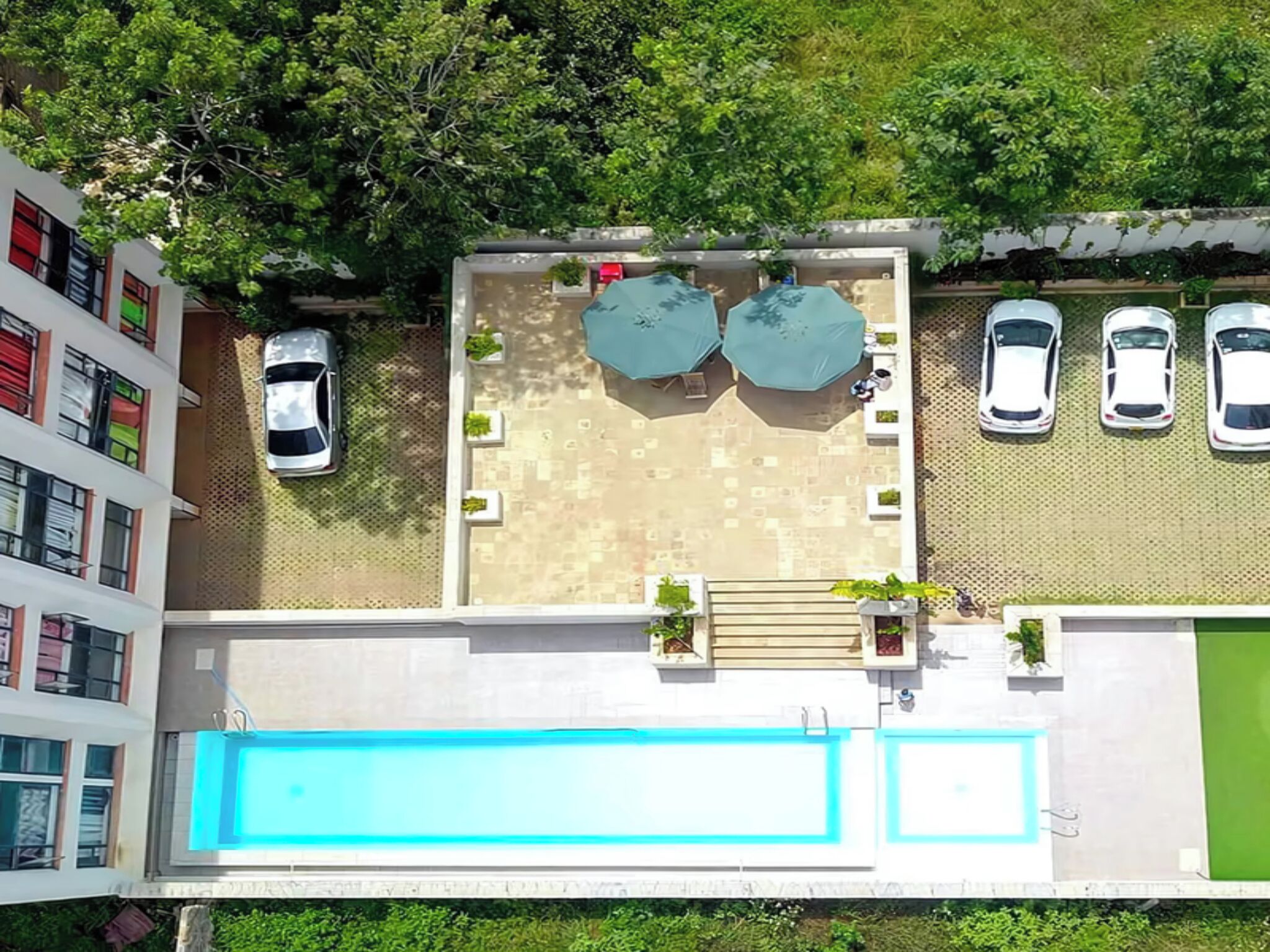Une vue aérienne d’un toit-terrasse avec une piscine, deux parasols et une rangée de voitures garées.
