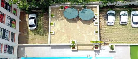 Une vue aérienne d’un toit-terrasse avec une piscine, deux parasols et une rangée de voitures garées.