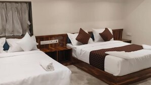 A hotel room with two beds, wooden headboards, white bedding, and a small bedside table with a lamp. - Hotel Sanjary International (Mumbai)