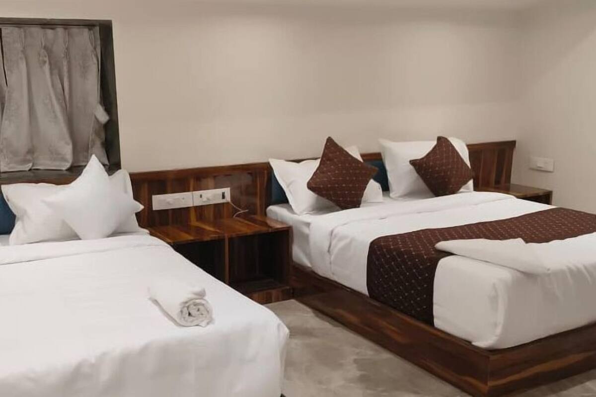 Une chambre d’hôtel avec deux lits, des têtes de lit en bois, du linge de lit blanc et une petite table de chevet avec une lampe.