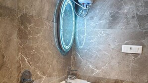 A bathroom with a marble wall, a wall-mounted sink, a towel rack, and a hand dryer. - Hotel Sanjary International (Mumbai)