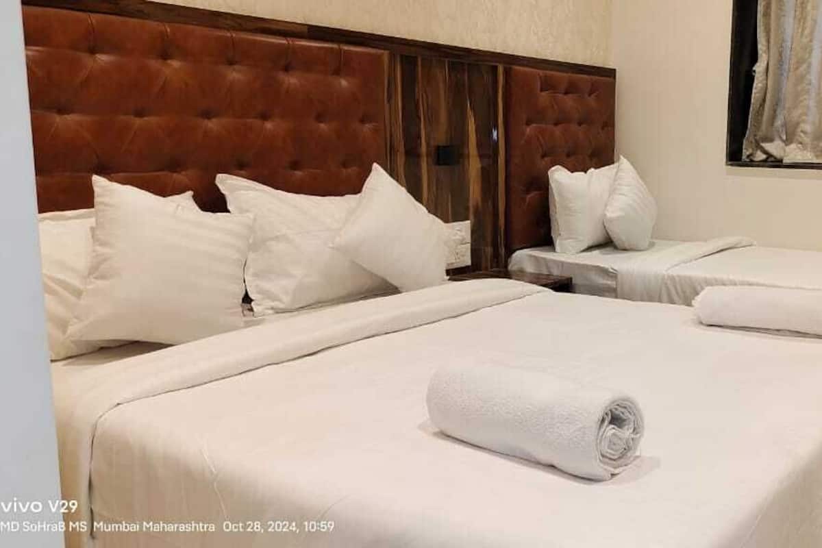 Une chambre d’hôtel avec trois lits, chacun doté de draps et d’oreillers blancs, d’une tête de lit capitonnée et d’une fenêtre avec des rideaux.