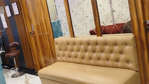 A room with a wooden door, a cushioned bench, a chair, and a patterned wall. - Hotel Sanjary International (Mumbai)