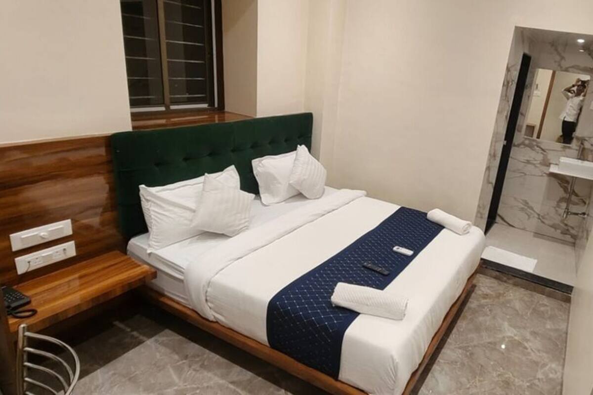 Une chambre d’hôtel avec un lit, une table de chevet, un miroir et une salle de bain visible à travers une porte ouverte.