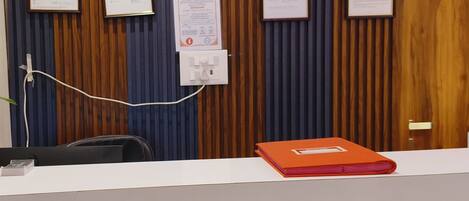 A reception desk with framed documents, a sign indicating advance check-out time, and a power outlet.