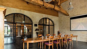 A dining area with a long wooden table, several chairs, and a projector screen on the wall. - Villa Héloise (Puisseguin)