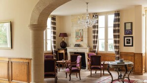 A spacious room with a fireplace, wooden furniture, and a chandelier. - Villa Héloise (Puisseguin)