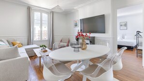 A modern living room with a round white table, clear plastic chairs, a sofa, and a flat-screen TV mounted on the wall. - Apartments in Champigny-Sur-Marne - 30 minutes from Disneyland (Champigny-sur-Marne)