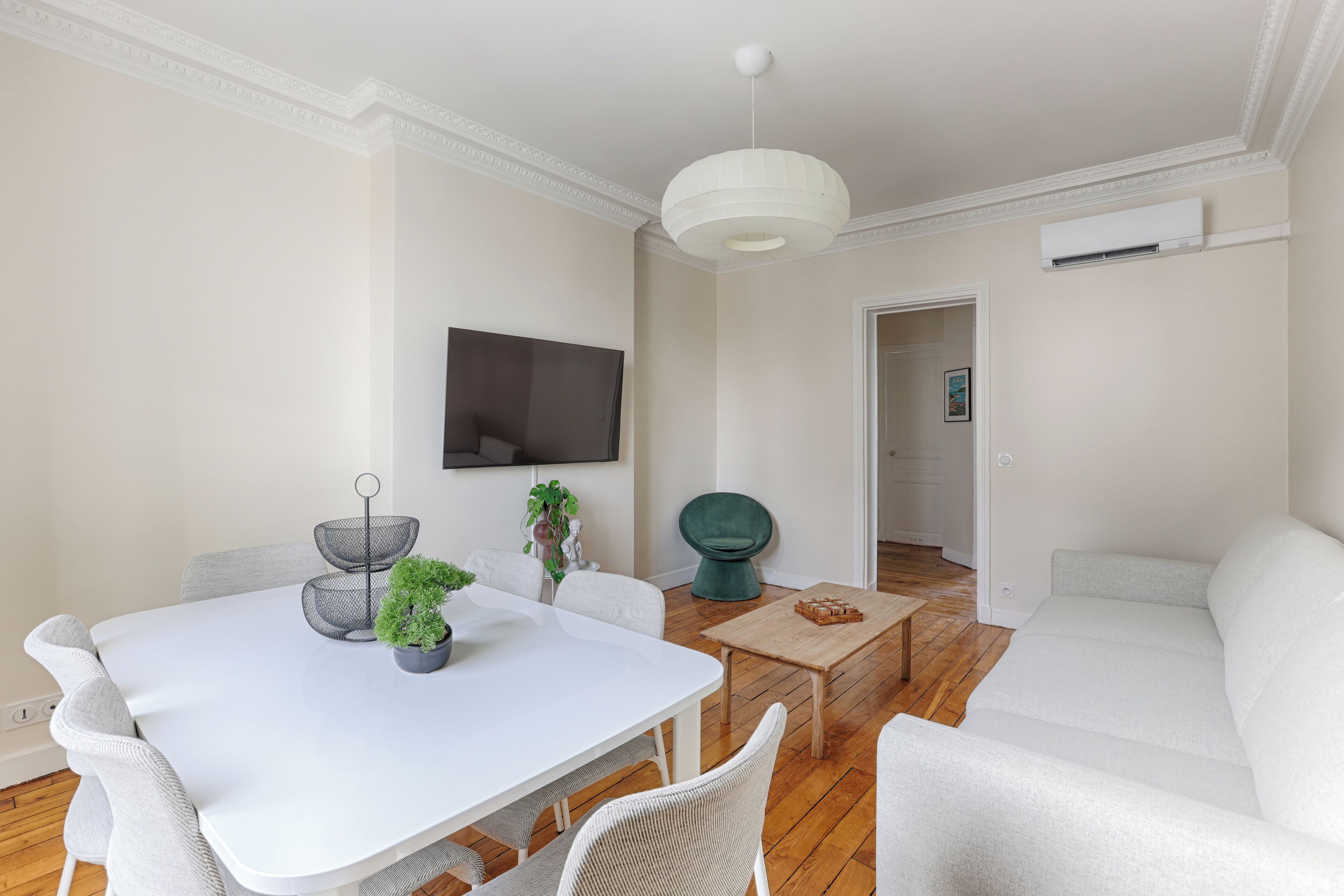 A modern living room with a white sofa, a dining table with chairs, a green chair, and a wooden coffee table.