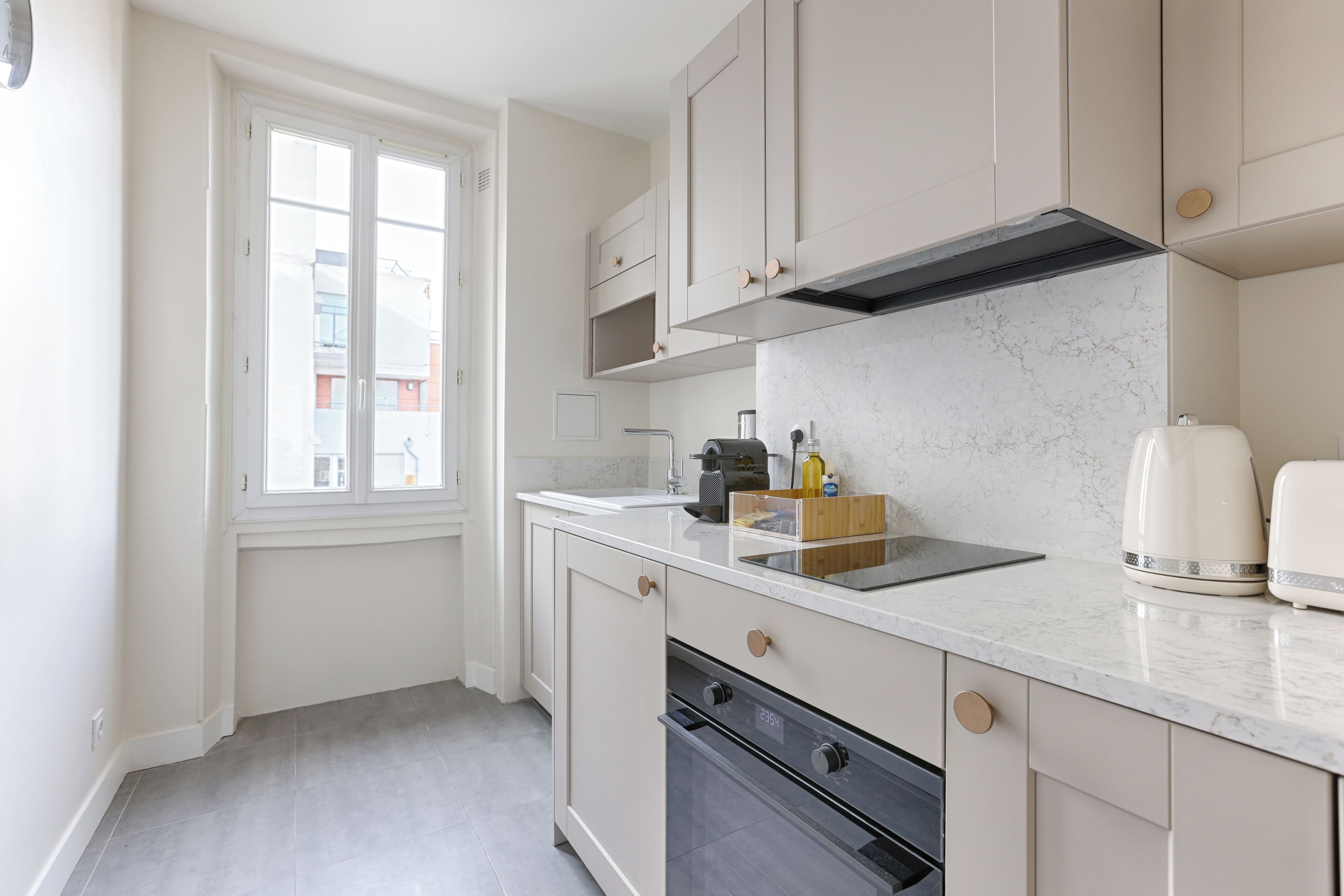 Une cuisine moderne dotée d’une grande fenêtre, de meubles blancs, d’un four encastré et d’un plan de travail en marbre.