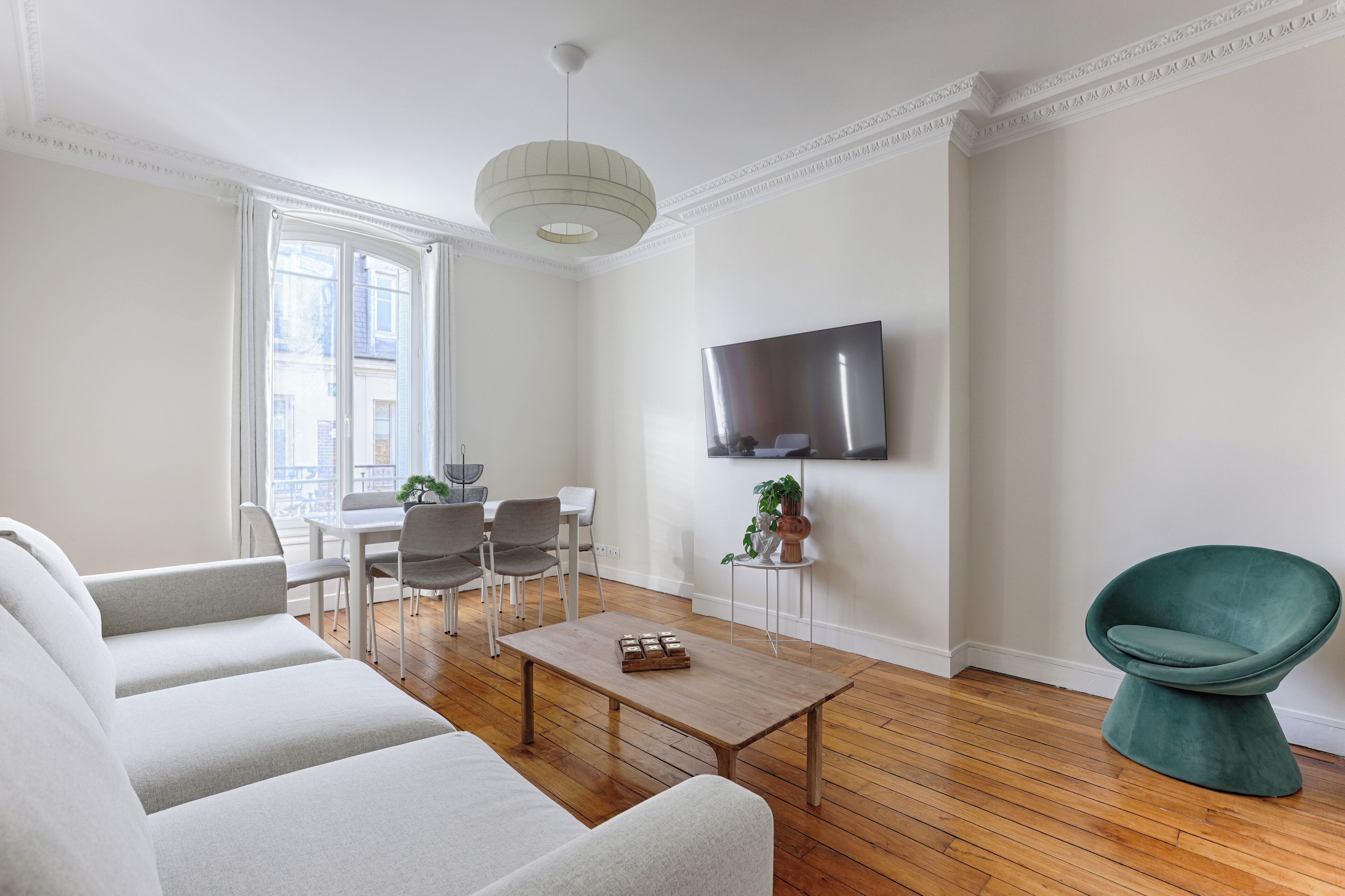 A modern living room with a sofa, dining table, chairs, a coffee table, a TV, and a potted plant.