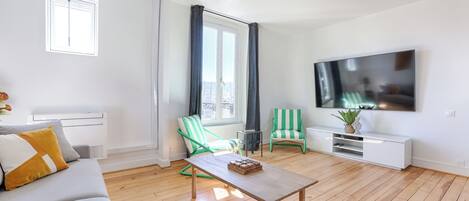 A modern living room with a sofa, two striped chairs, a coffee table, a TV, and a large window with curtains.