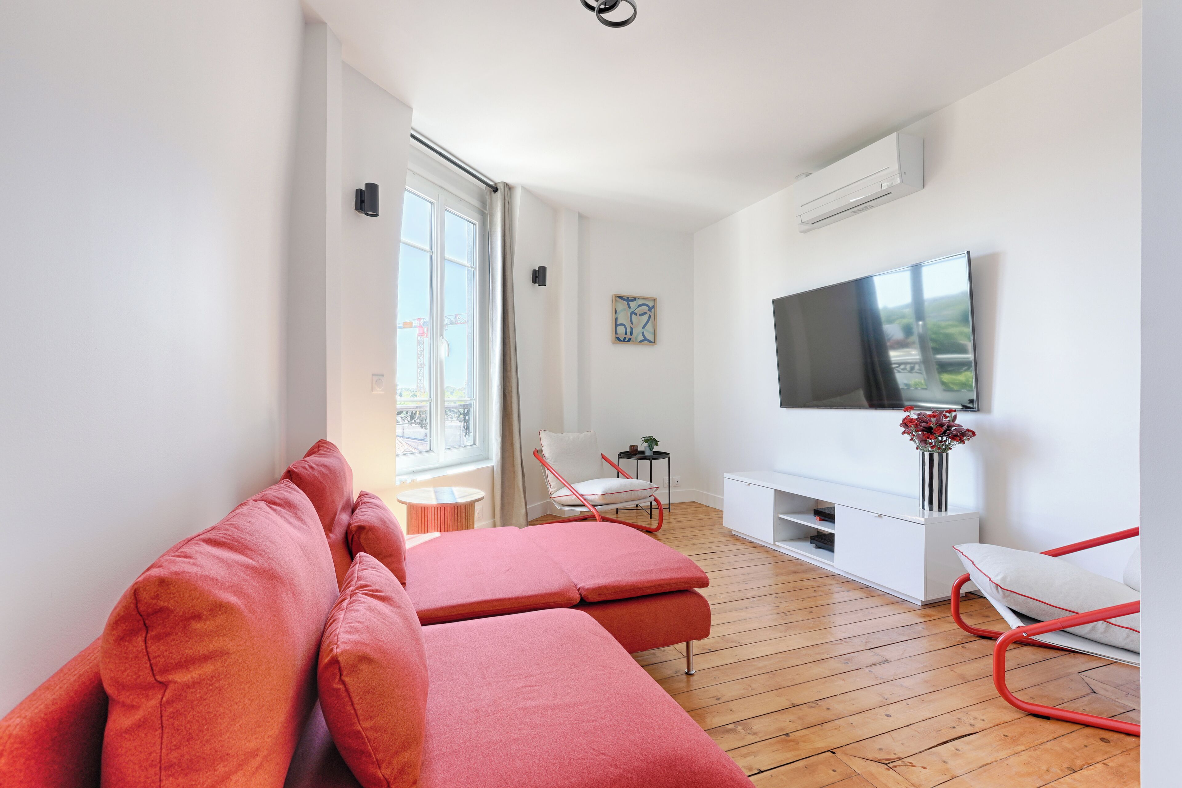 Ein modernes Wohnzimmer mit einer Couch, einem Sessel, einem Fernseher und einem kleinen Tisch mit einer Pflanze.