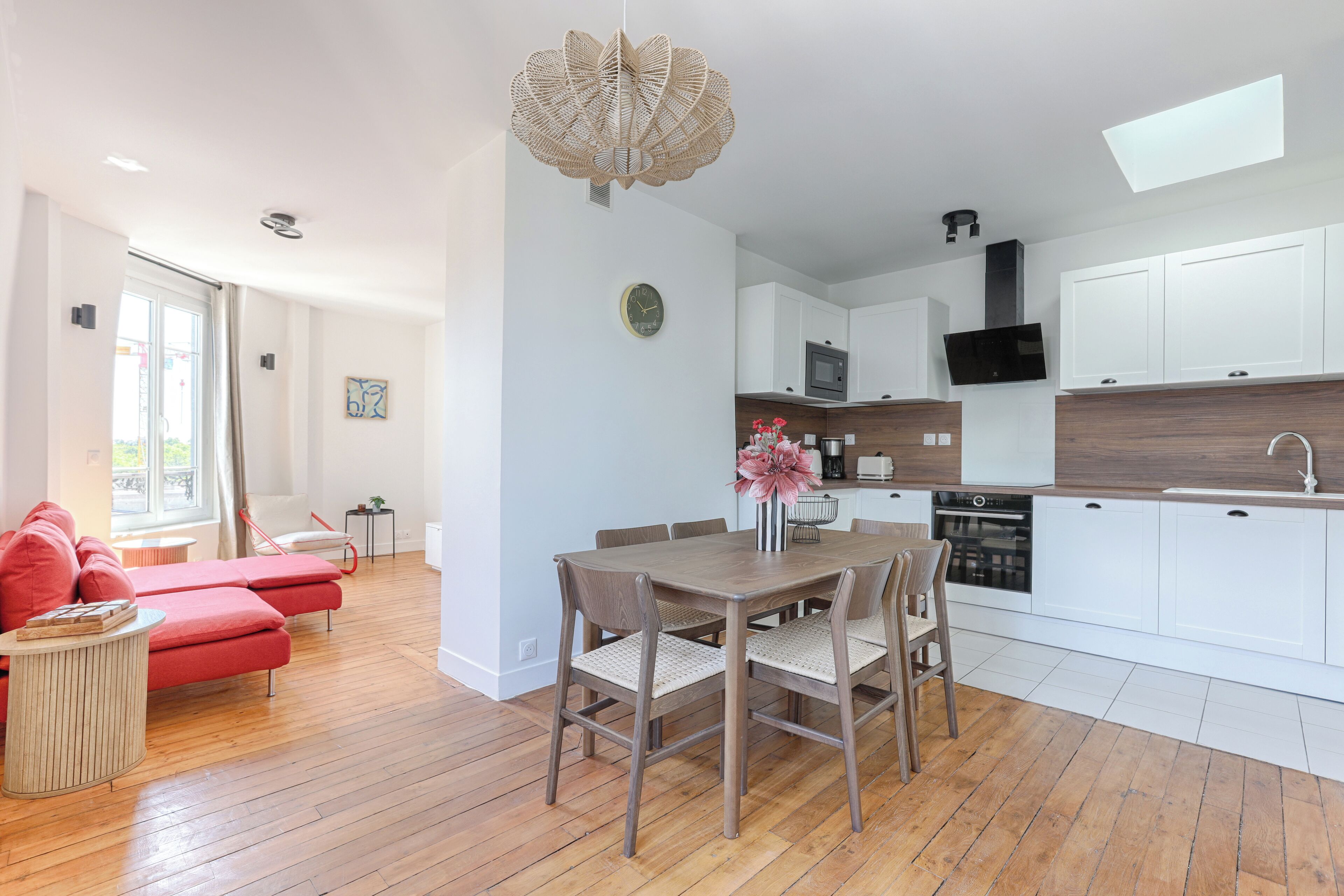 Une cuisine moderne avec des meubles blancs, une table à manger avec des chaises et un canapé rouge dans l’espace salon.