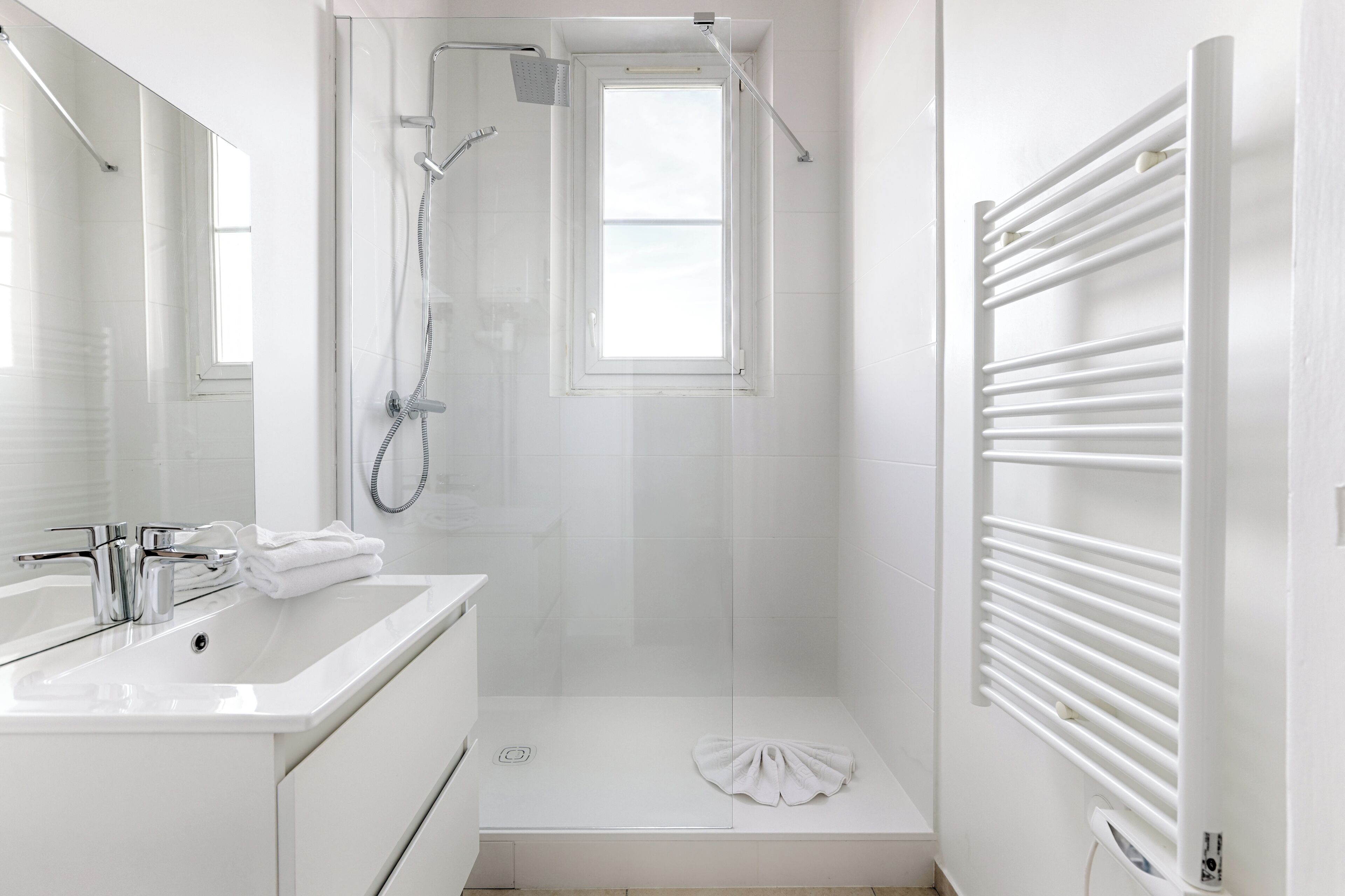 Een moderne badkamer met een douche, wastafel en handdoekrek.