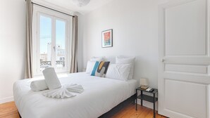 A neatly made bed with white linens and a towel, a small bedside table with a lamp, and a framed picture on the wall. - Apartments in Champigny-Sur-Marne - 30 minutes from Disneyland (Champigny-sur-Marne)
