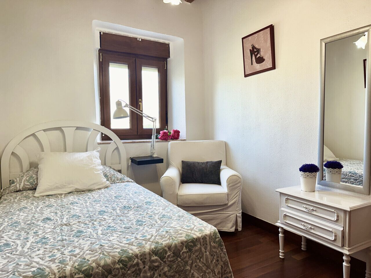 Ein Schlafzimmer mit Bett, Sessel, Schminktisch und Spiegel, mit Blick aus dem Fenster.