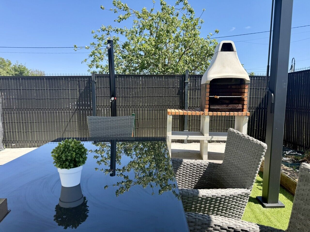 Une terrasse avec une table, des chaises en osier, une plante en pot et un barbecue en briques.