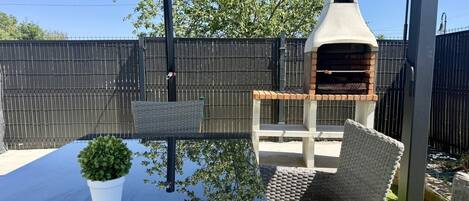 Une terrasse avec une table, des chaises en osier, une plante en pot et un barbecue en briques.