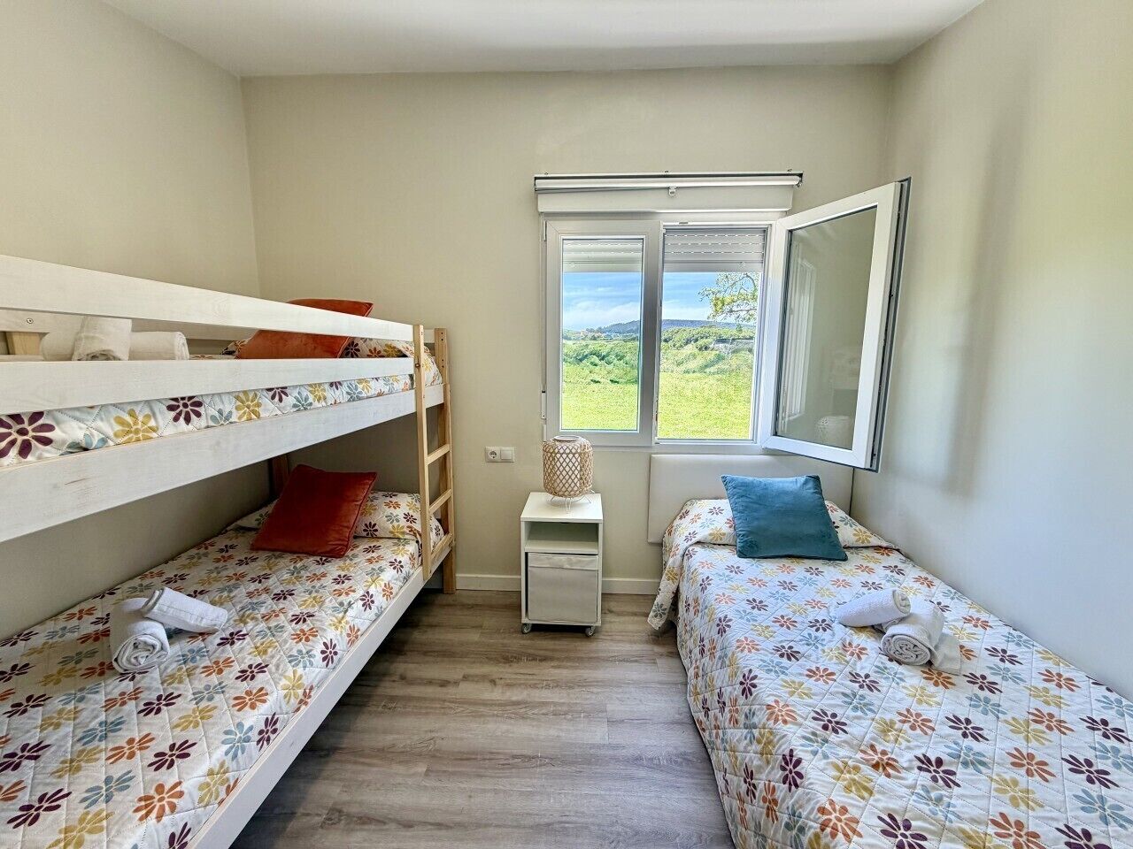 A small, well-lit room with two single beds, a window with a view, and a small table.