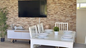 Ein Essbereich mit Backsteinwand, einem flachbildfernseher über dem Tisch, weißen Stühlen und einem weißen Konsolentisch mit Topfpflanze und Dekoration.