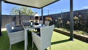 Eine Terrasse im Freien mit Tisch, Stühlen, einem Grill und einem überdachten Bereich.