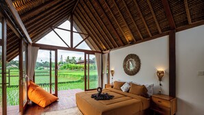 A bedroom with a large bed, wooden flooring, a view of a rice field, and a thatched roof. - Pondok Mawas (Ubud)