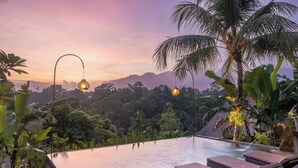 An infinity pool with lounge chairs, surrounded by tropical plants and palm trees, overlooking a lush landscape. - Pondok Mawas (Ubud)