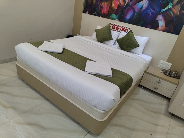 A neatly made bed with white and green bedding, a headboard with a decorative pattern, and a bedside table with a lamp and a cup.