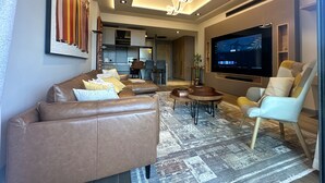 A modern living room with a leather sofa, a patterned rug, a TV, and a dining area with chairs and a table. - Charming 1-bedroom condo at The Diamond In City, Cantonments Accra. Luxe-Modern (Accra)