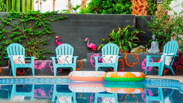 Un área de piscina con sillas Adirondack azules, anillos inflables y una estatua de Buda.