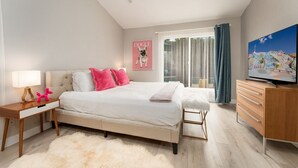 A bedroom with a bed, bedside table, lamp, and a TV. - Palm Springs Chic Retro Retreat w Pool/Spa/Games (Palm Springs)