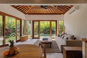 A spacious living area with a large sofa, wooden coffee table, and a dining table with fruits. - Kilani  Villa By Betterplace (Pecatu)