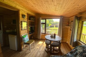 A wooden cabin interior with a dining table, chairs, a refrigerator, and a television.