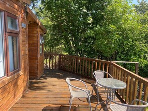 A wooden deck with two wicker chairs and a table, surrounded by a wooden railing, overlooking a wooded area. - Lakeside Lodge - Castlemartyr - Sleeps 4 (Castlemartyr)