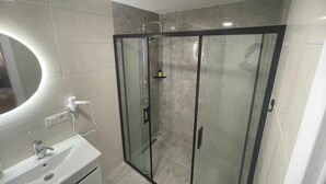 Un baño moderno con ducha envuelta en vidrio, un lavabo blanco y un espejo sobre el lavabo.
