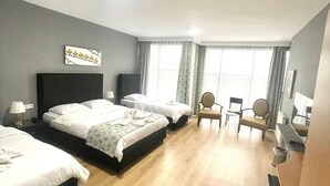 Habitación de hotel con tres camas, un escritorio, una silla y un ventanal con cortinas.