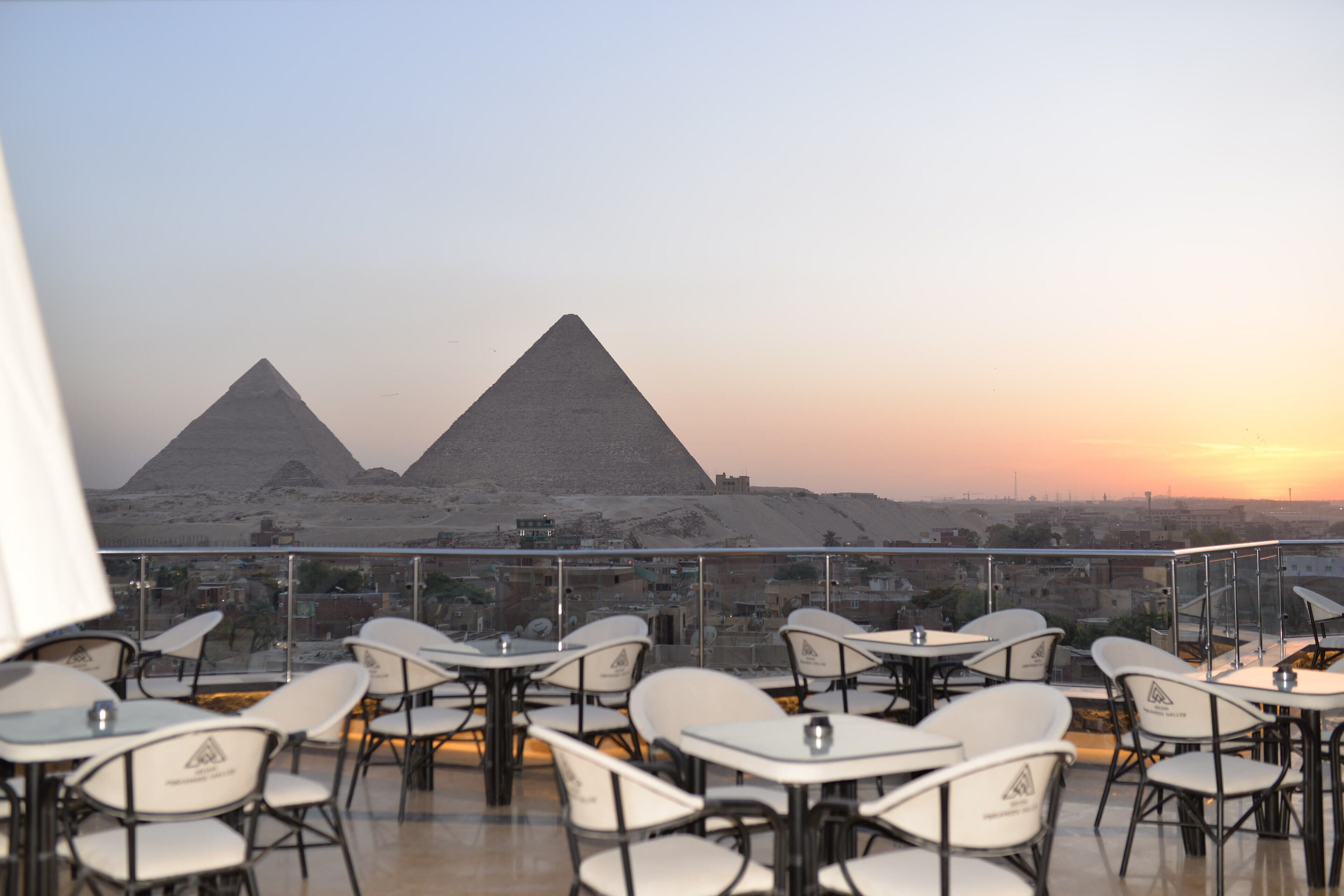 Una terrazza sul tetto con tavoli e sedie, che offre vista sulle piramidi al tramonto.