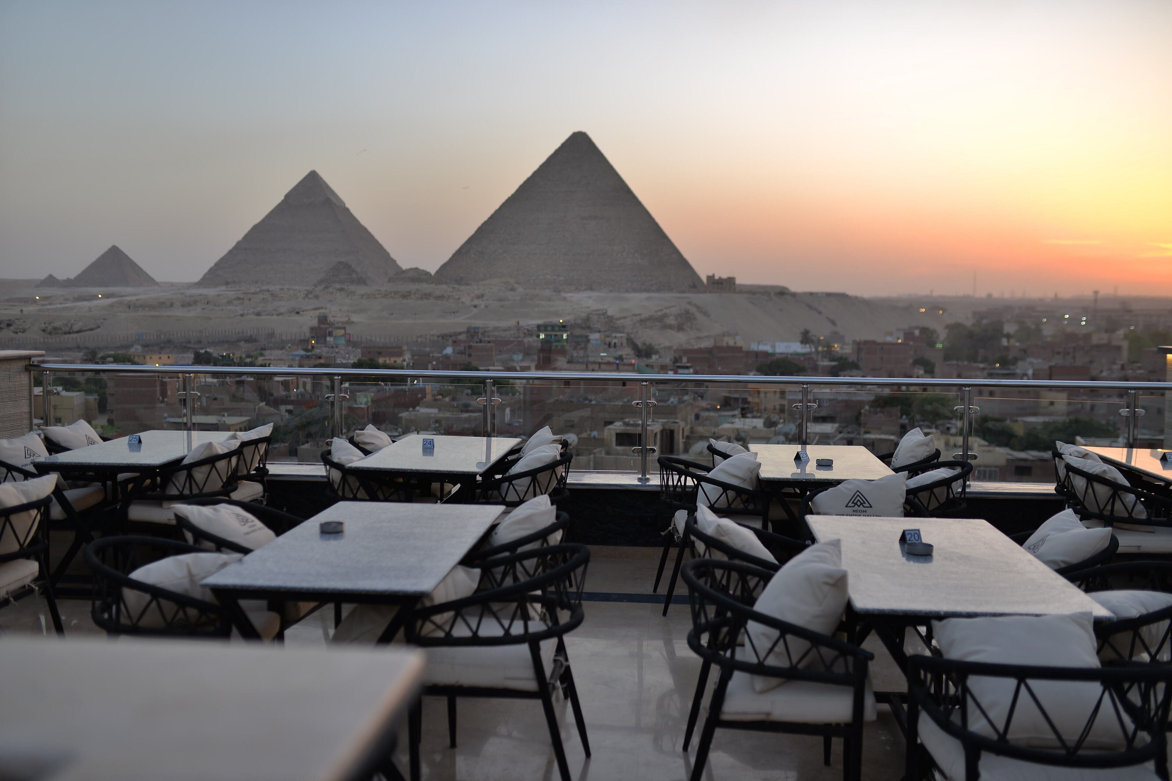 A rooftop terrace with tables and chairs, offering a view of the pyramids.