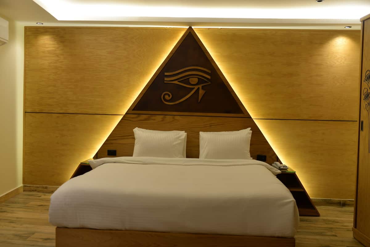 A modern hotel room with a wooden headboard, a bed with white linens, and a decorative wall panel featuring an eye symbol.