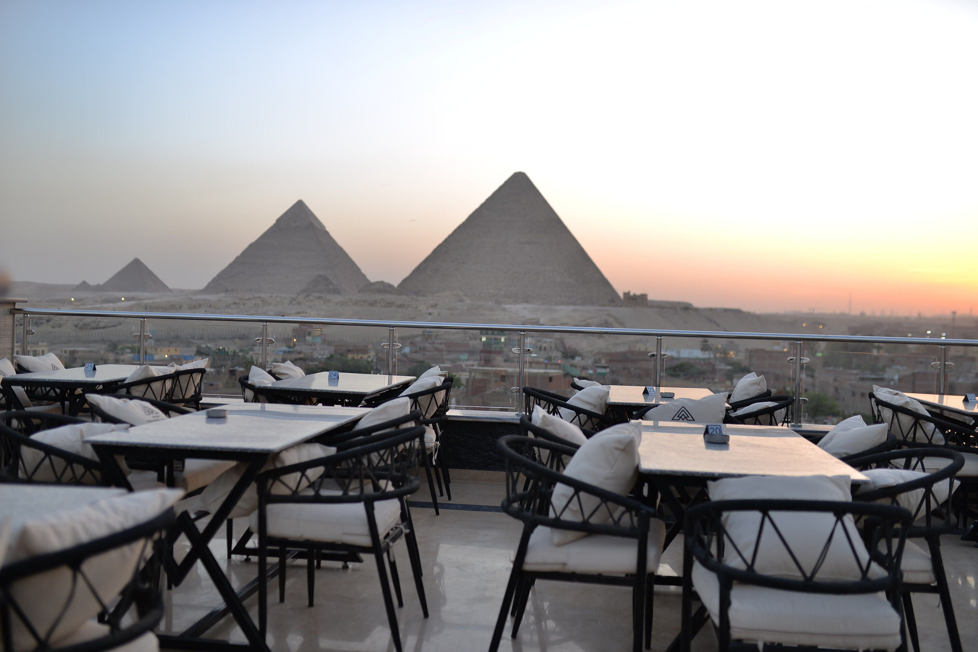 An outdoor seating area with tables and chairs, overlooking a view of the pyramids.
